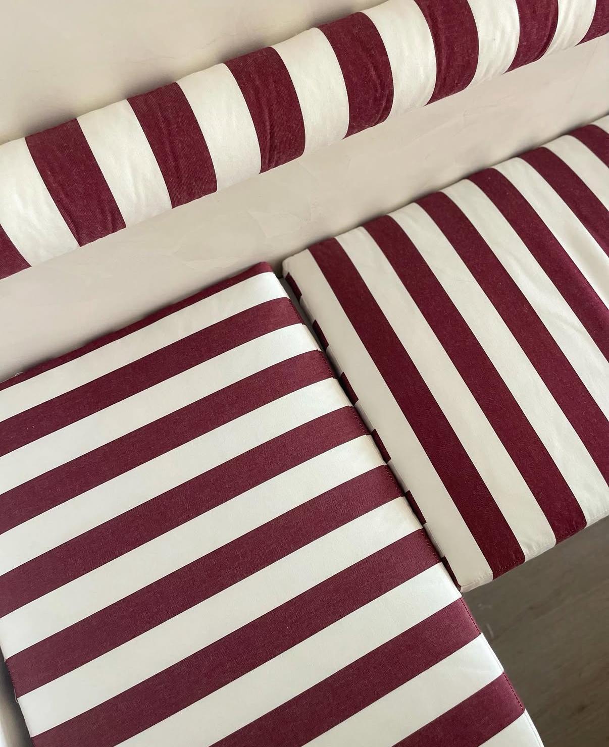 Detalle de almohadones a rayas blancas y bordó sobre banco de obra