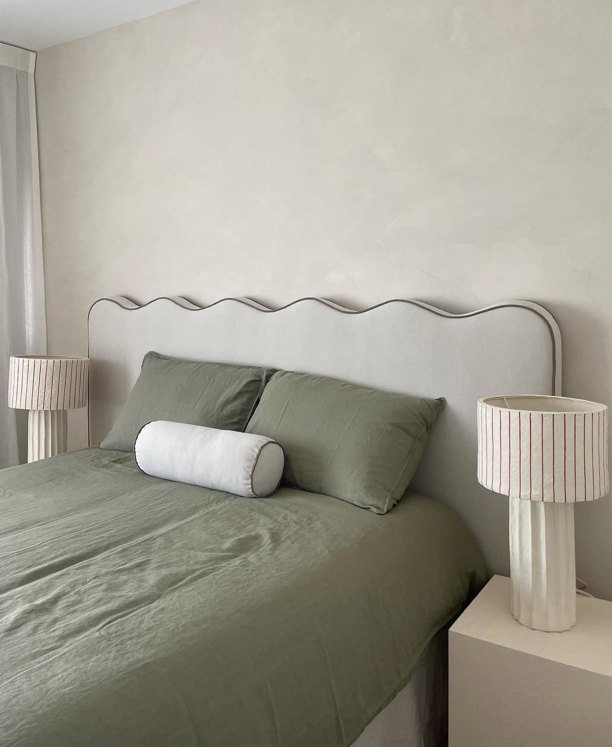 Dormitorio con respaldo ondulado tapizado, ropa de cama verde salvia y lámparas de mesa de lino