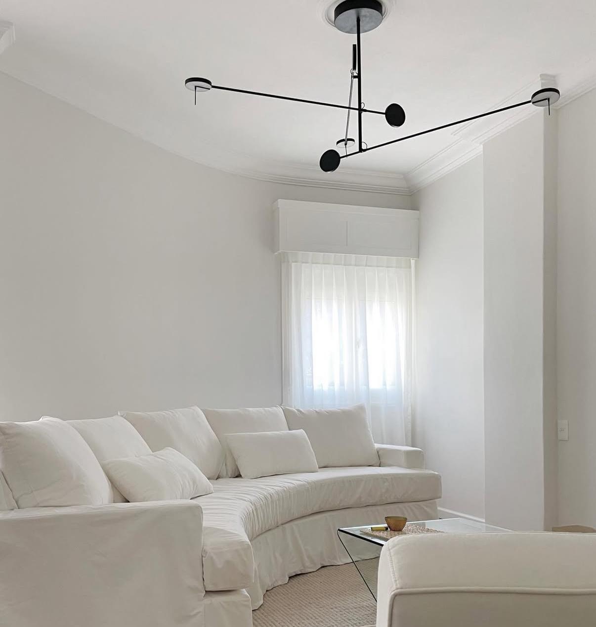 Sala de estar en blanco roto con sofá seccional, cortinas de voile y lámpara de techo negra de brazos articulados